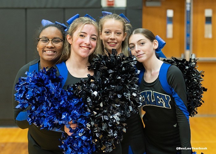 Image of 4 high school cheerleaders gathered together looking at the camera while holding their pom poms