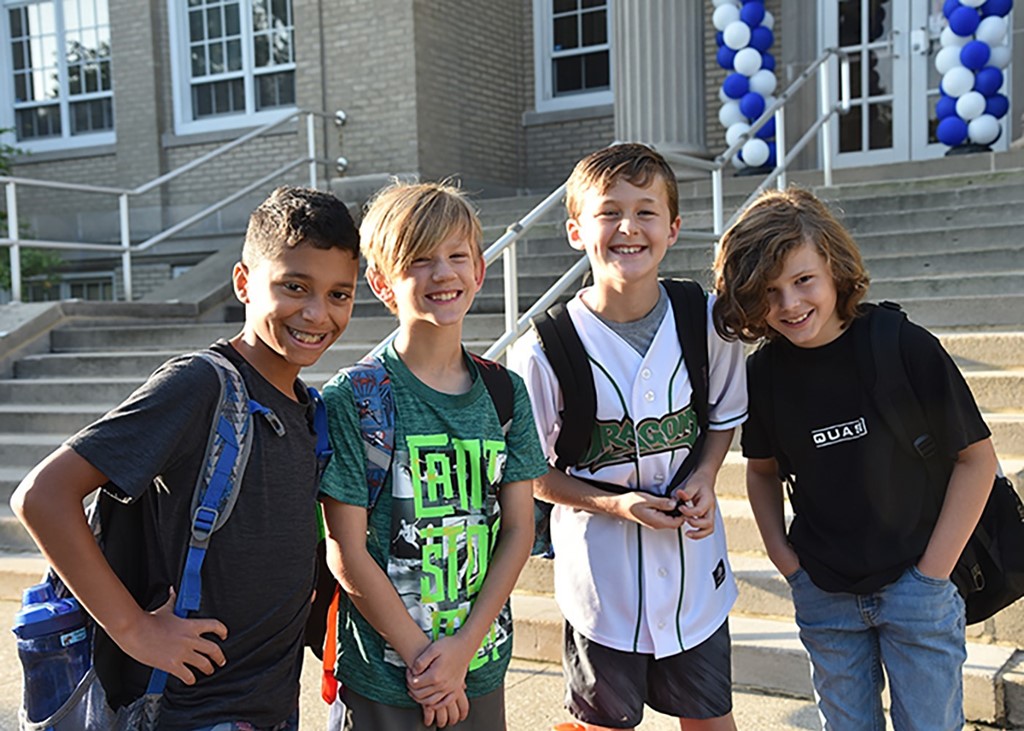 Image of 4 young boys posing for the camera and standing in front of the steps of Montrose Elementary School on the first day of school