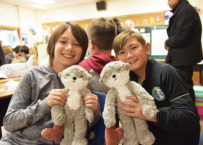 Image is of 2 young elementary-aged boys who are side by side and holding a stuffed toy