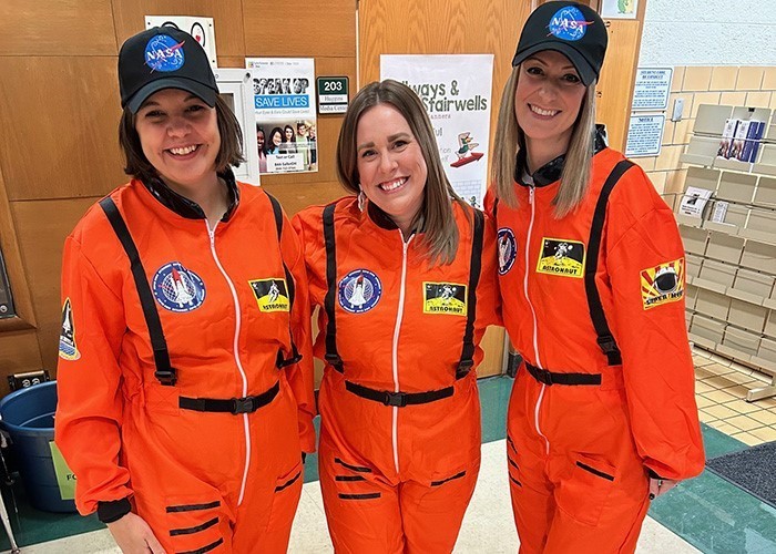 Image is of 3 female teachers standing side by side while each wearing bright orange NASA astronaut uniforms