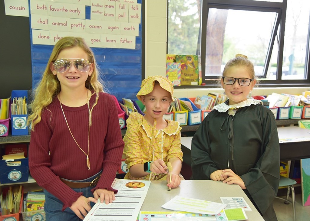 Image of 3 young elementary girls standing side by side in a classroom while dressed up as historical figures